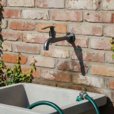 Robinet pour exterieur Arrosage Optimal+ au mur d'une maioson de brique avec boyau vert