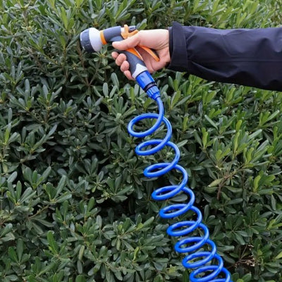 Tuyau arrosage extensible FlexiBlue bleu en spirale, gros plan main tenant un pistolet multijet orange/gris devant une haie